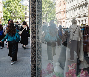 A group of people seen from behind walking on the sidewalk. Reflectiong in the shopping window.