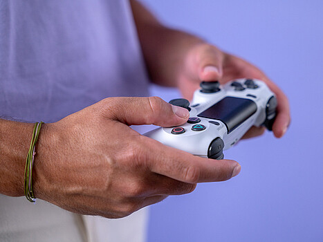 Two hands holding a game controller, with a purple background.