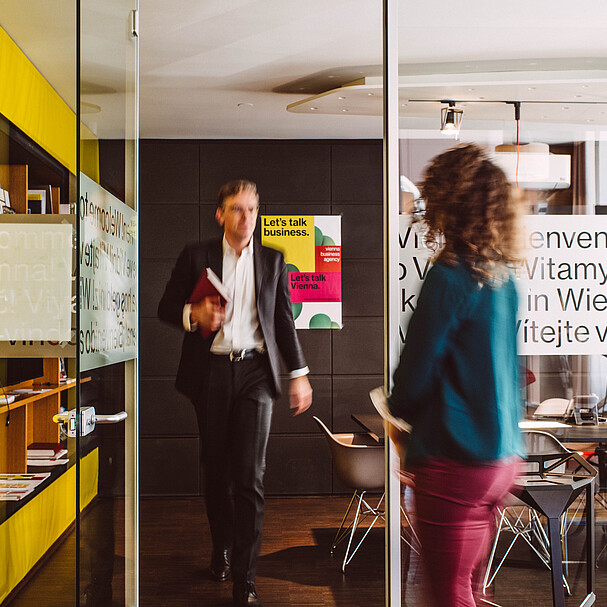 Man exiting a meeting room, walking towards a woman waiting in front