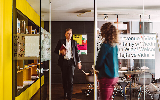 Man exiting a meeting room, walking towards a woman waiting in front