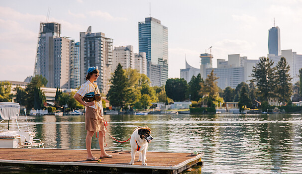 Woman with sunglasses and sportswear standing with dog on pier at Alte Donau