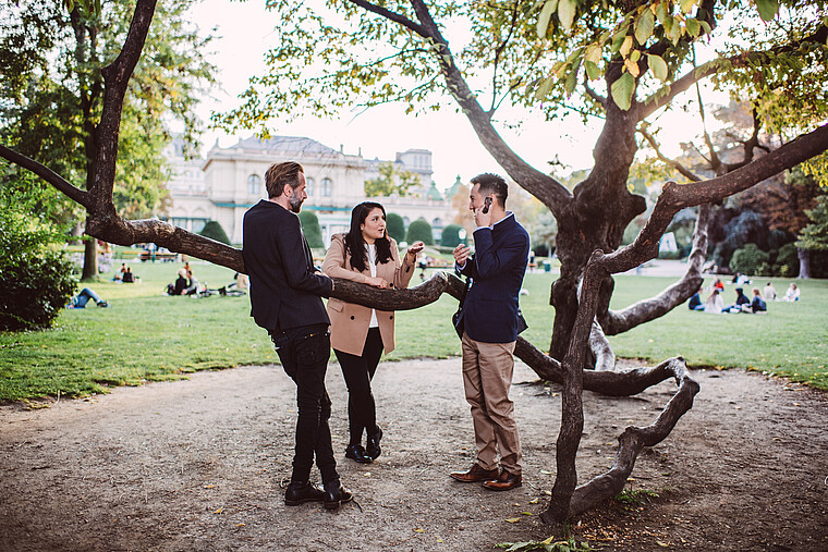 Two men and a woman standing in Stadtpark and speaking