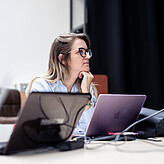 Digital events in Vienna A woman sitting at a desk in front of multiple laptops, engaged in conversation