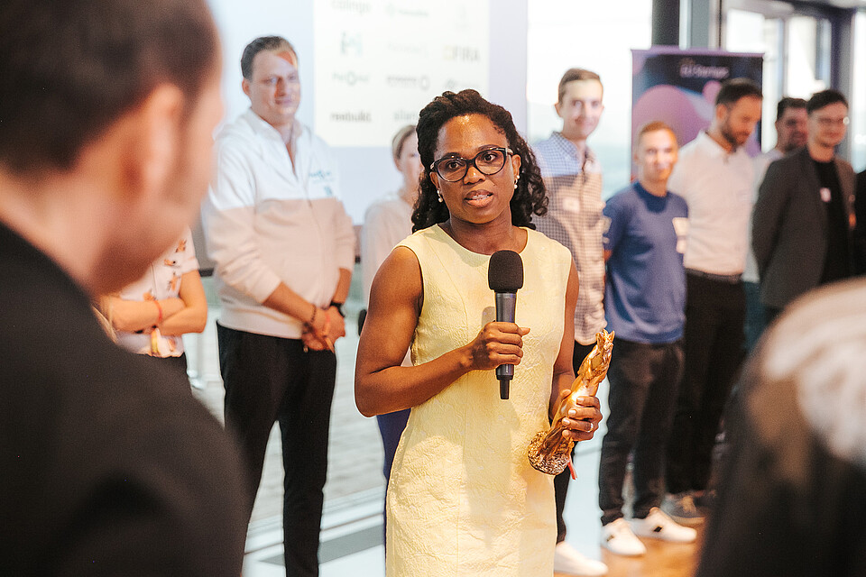 Woman in yellow dress speaking into a microphone to a group of people at a business event