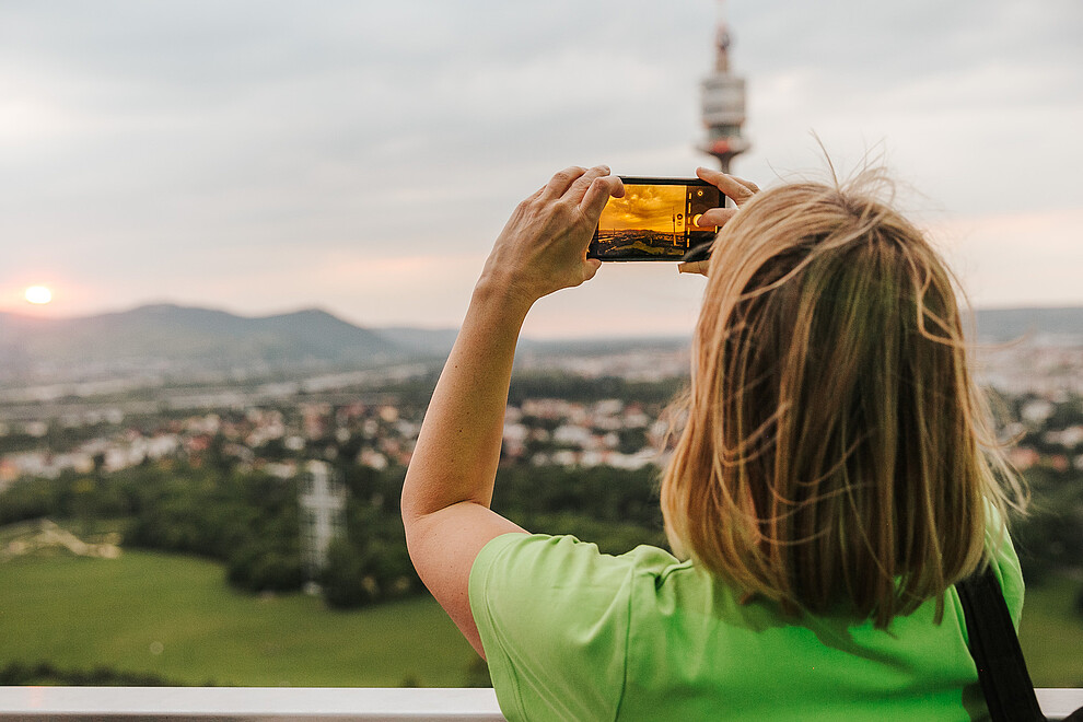 Woman in a green top taking a photo of a view of Vienna on her smartphone