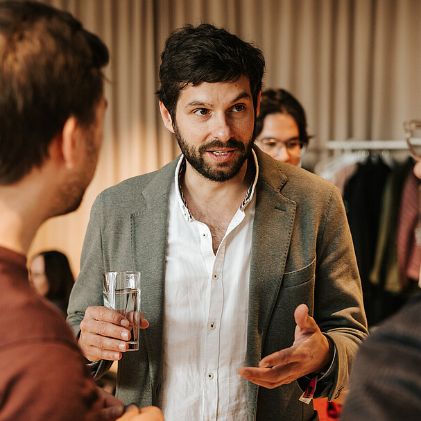 A man holding a glass of water talking to two other men