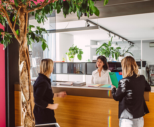 A receptionist talking to two women at a desk 
