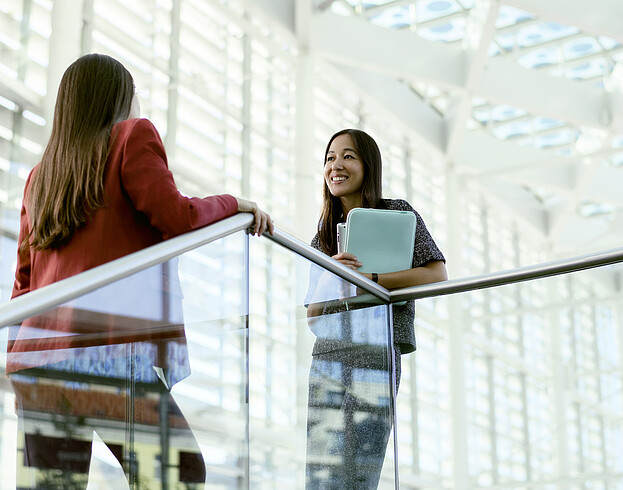 Two young women chat in a large white conference space.