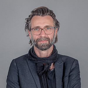 Gregor-Robert Posch, ein Mann mit graumelierten Haaren, Vollbart und Brille