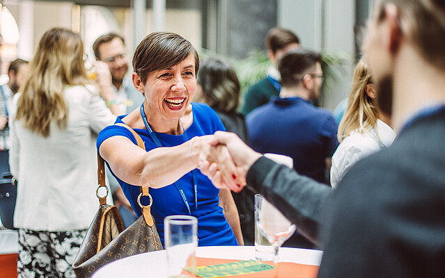 Woman with short hair in a blue dress shaking hands with a man