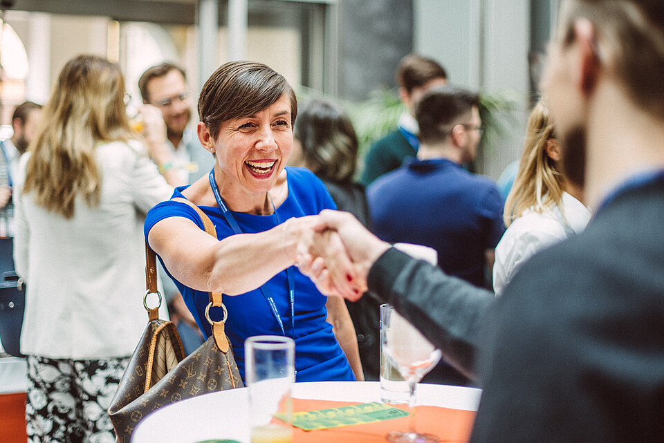 Woman with short hair in a blue dress shaking hands with a man