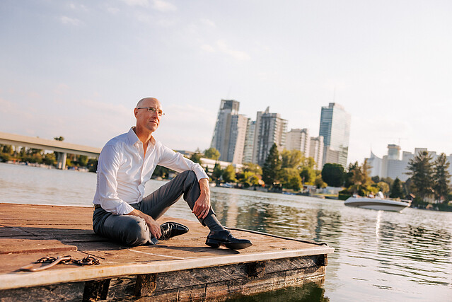 Man in white shirt sitting casually at pier and looking at the Donau