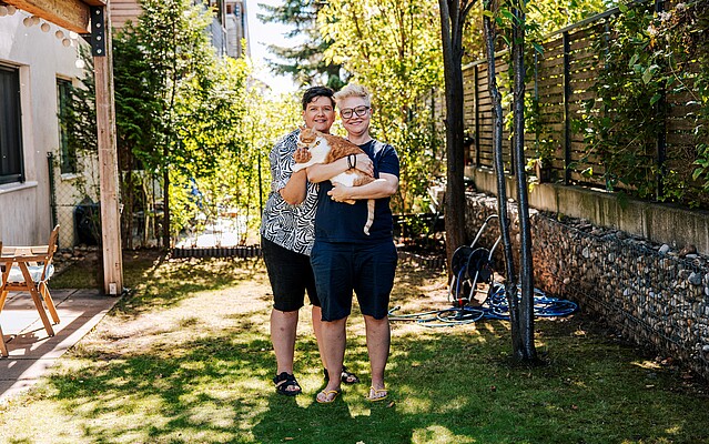 Two women smiling and holding an orange cat in a garden