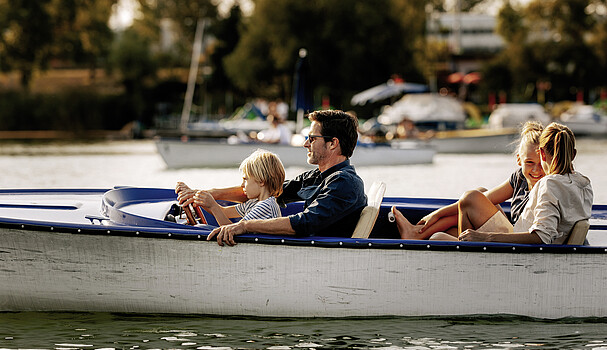 A laughing family rides in an electric boat on the Danube river.