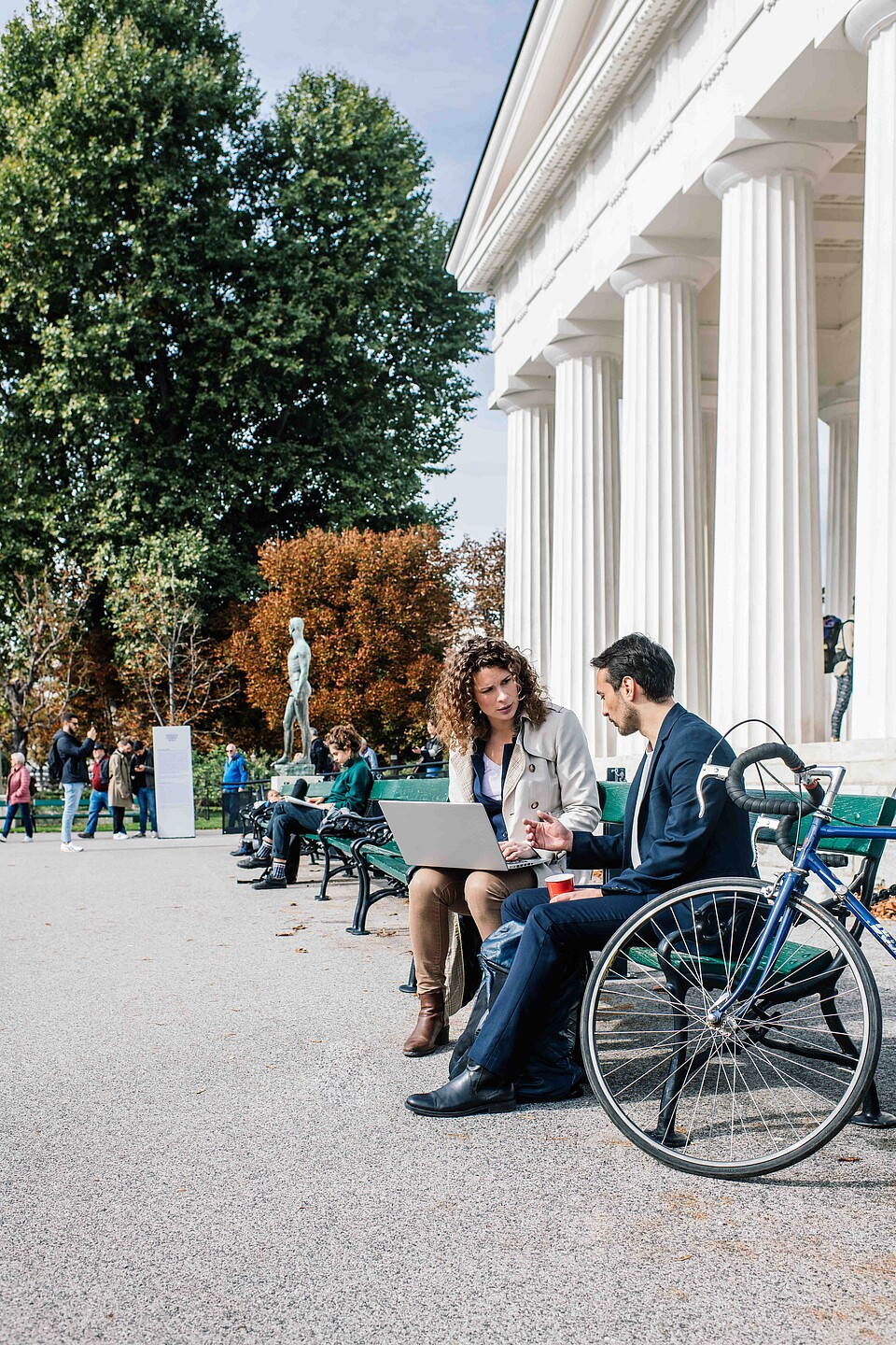 Man and woman sitting on a park bench looking at a laptop on a sunny day