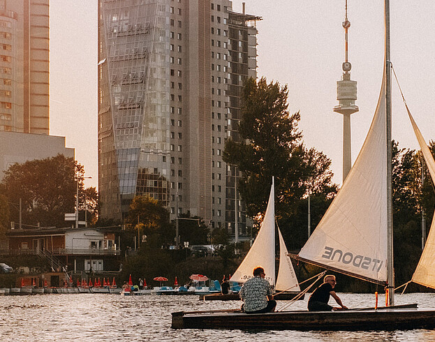 A boat sailing on a river with modern tower blocks in the background at sunset