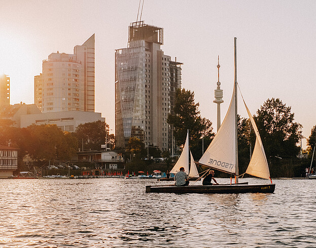 A boat sailing on a river with modern tower blocks in the background at sunset