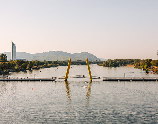A wide shot of the Danube river at sunset, with hills in the background, viewed from above. The photo was taken from a bridge.
