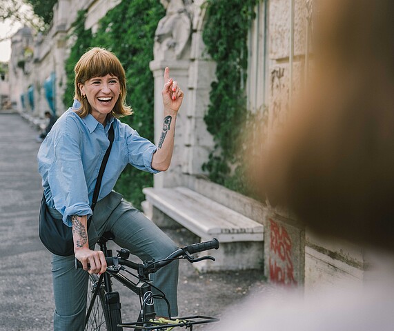 A young female startup executive is shown riding her bicycle in Vienna's Stadtpartk and waving to a friend.