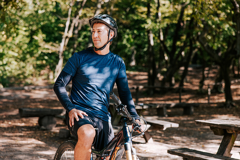 Male cyclist in a blue top and helmet on his bike surrounded by trees